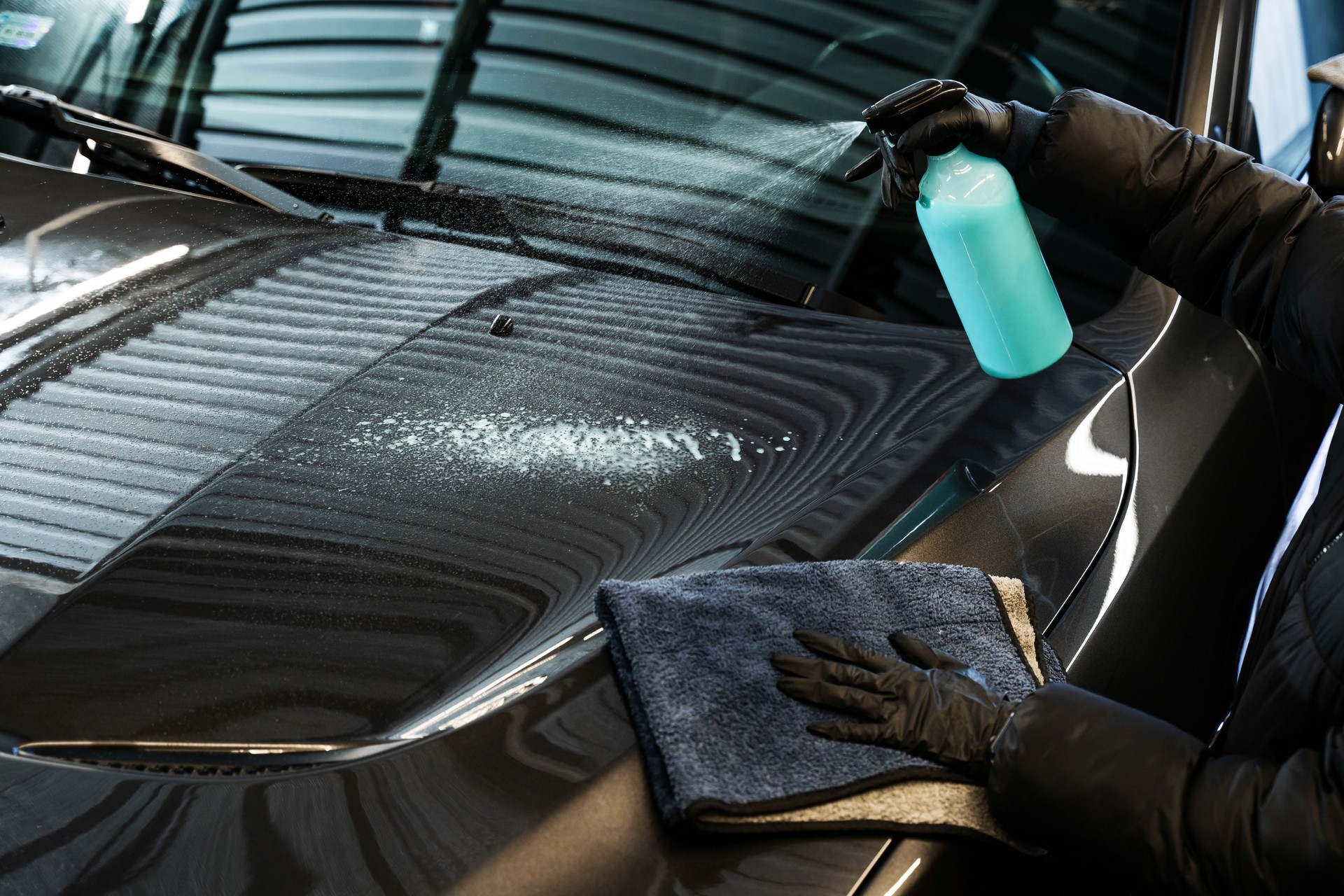 Polishing car body using microfiber cloth. Professional car valeting. Wiping vehicle after applying spray of quick detailer to make car surface clean and shining.